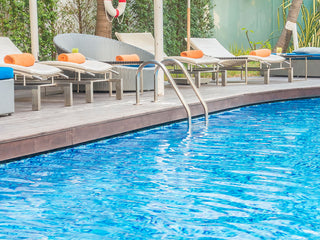 Hotel swimming pool with clear blue water and various lounge chairs.