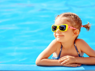 Young little girl with yellow glasses relaxing on edge of a pool.