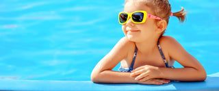 Young little girl with yellow glasses relaxing on edge of a pool.