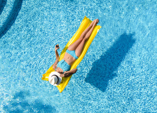 Women relaxing on a yellow float in a clear blue water swimming pool.