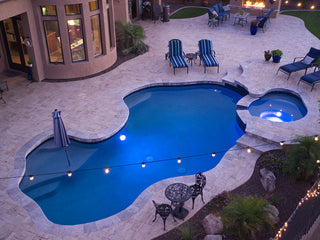 Evening view of an outdoor in-ground swimming pool with clear blue water and stone patio.