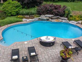Outdoor in-ground swimming pool with clear blue water, stone patio, and lounge chairs.