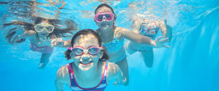 Children swimming in swimming pool with clear blue water.