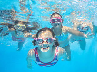 Children swimming in a clear blue water pool.