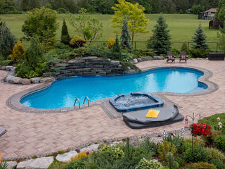 Outdoor in-ground swimming pool and spa with clear blue water and stone patio.